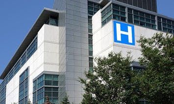 A modern, multi-story hospital building featuring large windows, a prominent blue 